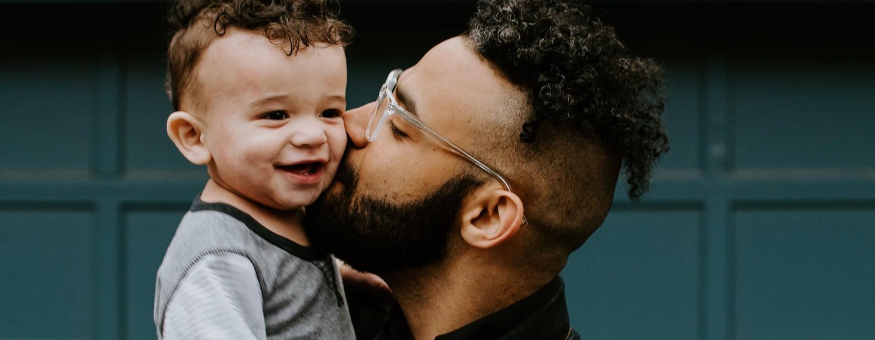 father holds and kisses his toddler son